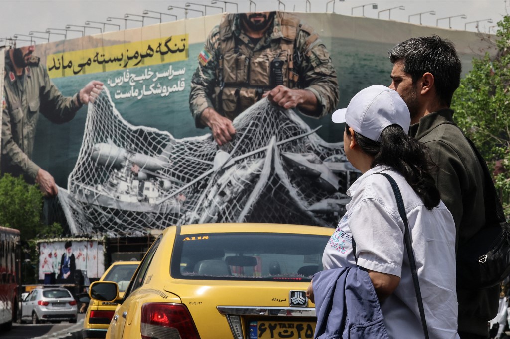 Iranian walks past a giant billboard reading 'The Strait of Hormuz remains closed' at the Revolution Square in Tehran on April 22, 2026.