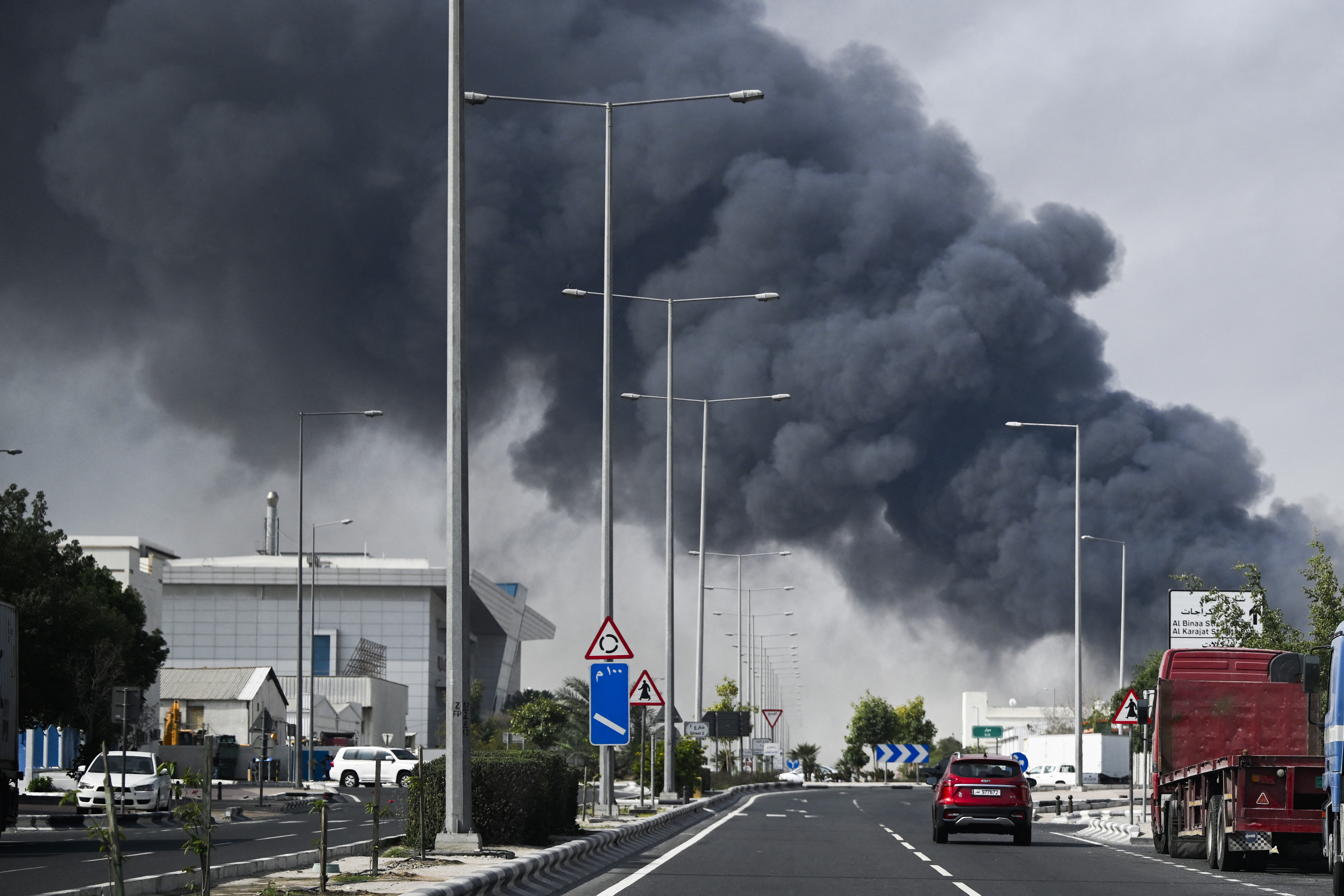 Motorists drive past a plume of smoke rising from a reported Iranian strike in the industrial district of Doha