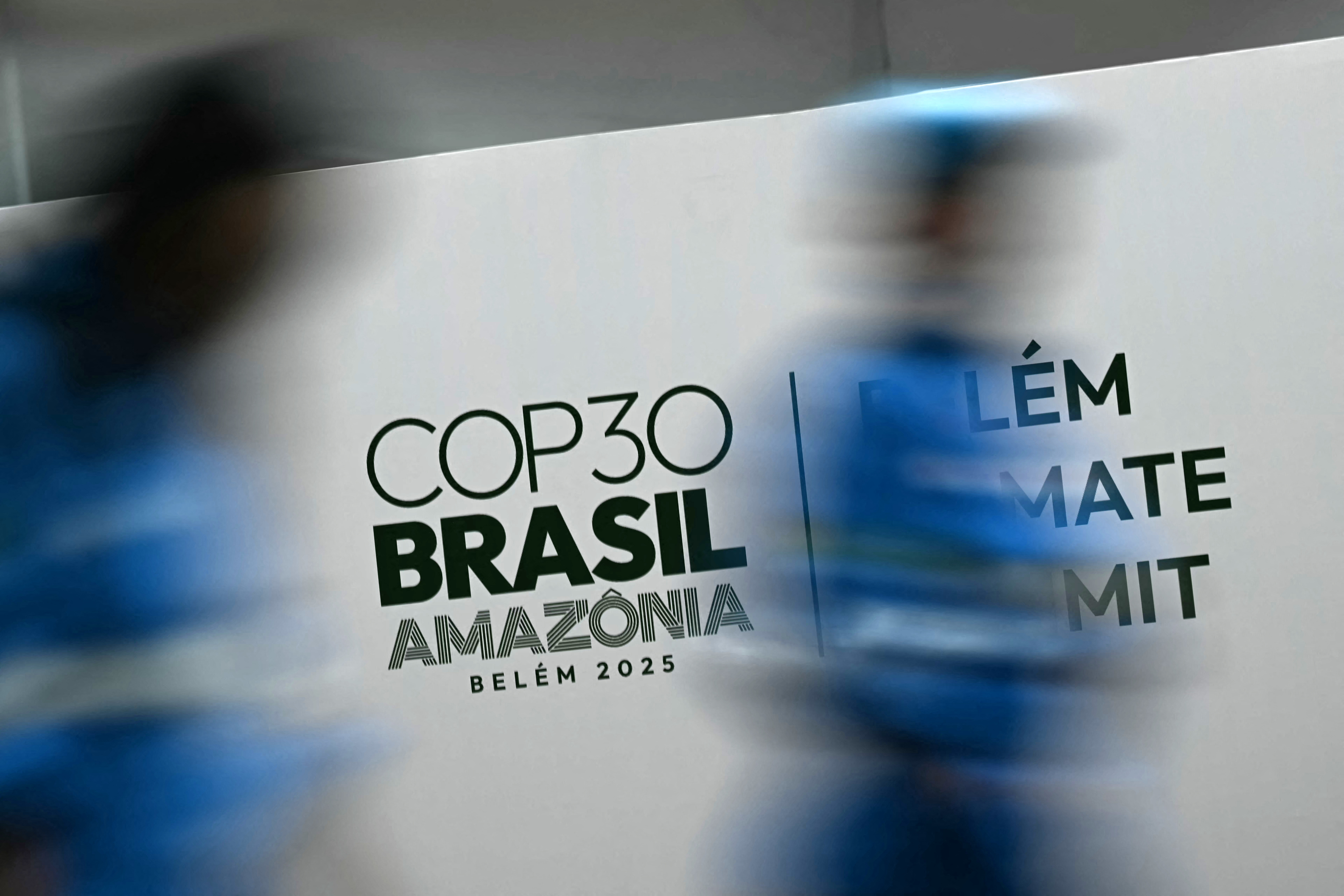 Workers walk past a banner with the COP30 UN Climate Change Conference