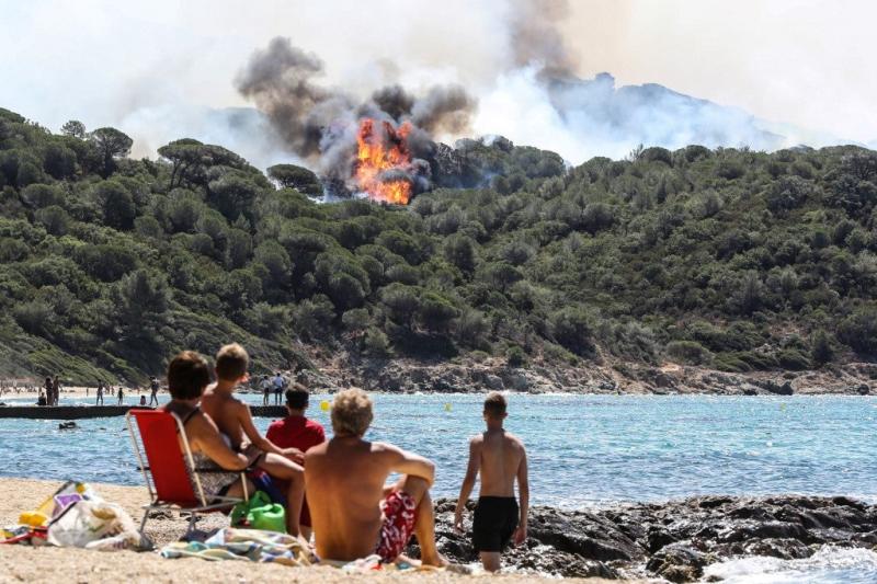 Personas disfrutan de la playa mientras miran un incendio forestal en La Croix-Valmer, cerca de Saint-Tropez, el 25 de julio de 2017. Valery HACHE / AFP