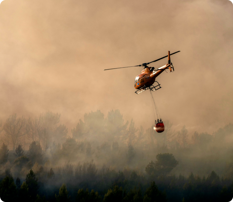 This photograph shows a firefighter Airbus Helicopters H125 helicopter flying over a wildfire raging in Pouzols-Minervois
