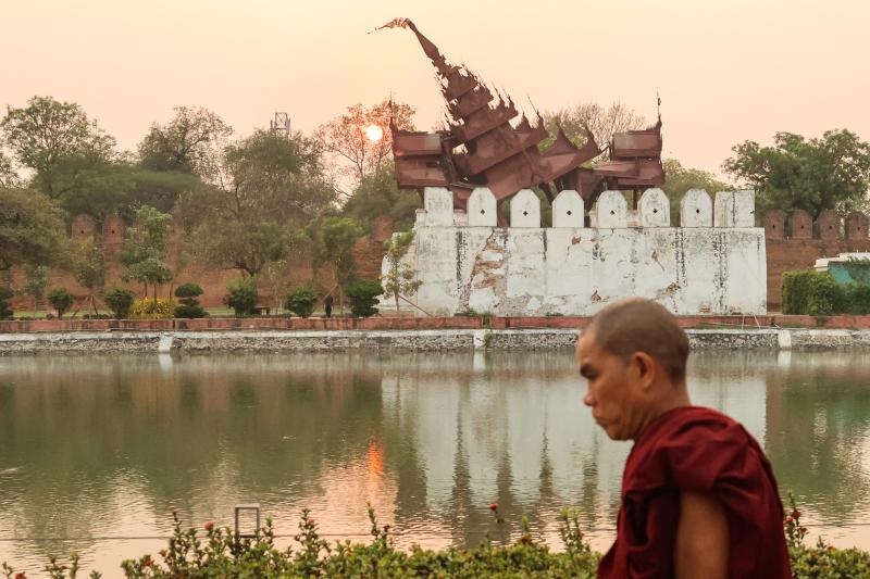 A Buddhist monk walks past the damaged Mandalay Palace